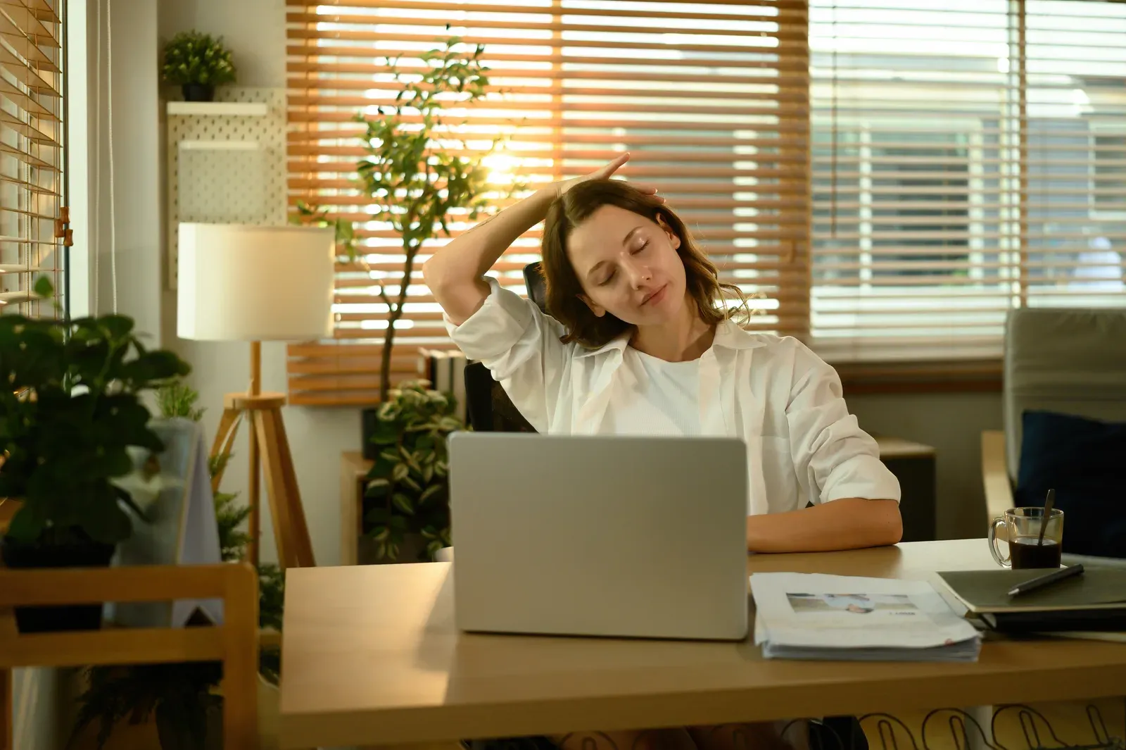 Woman gently stretching her neck at a desk with a laptop, a simple break for forward head posture