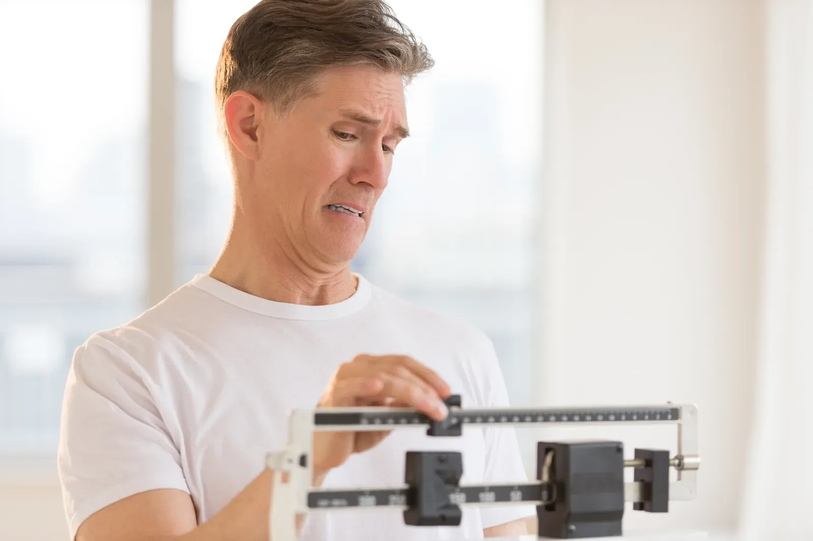 Worried man stepping on a weight scale at the gym, a common moment when weight rises after starting to train