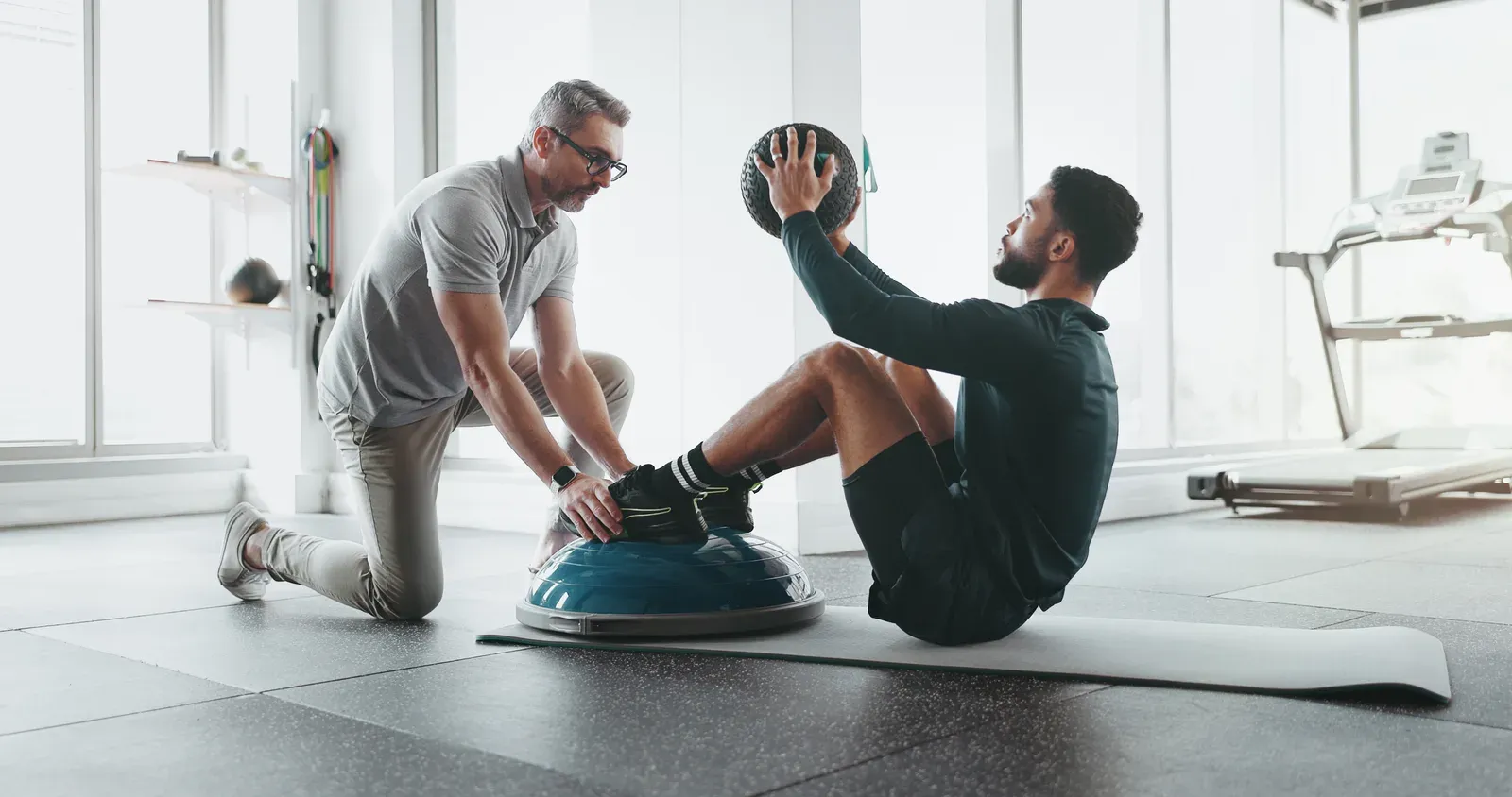 Personal trainer with a medicine ball in the gym, coaching that can make training fit a busy life in your 30s