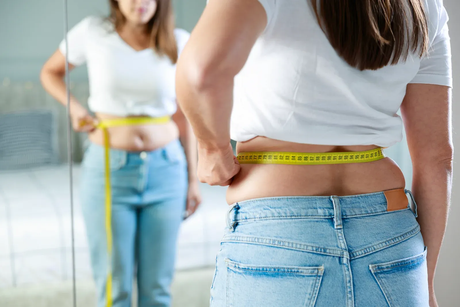 Young woman taking body measurements in front of the mirror in her bedroom, tracking waist changes