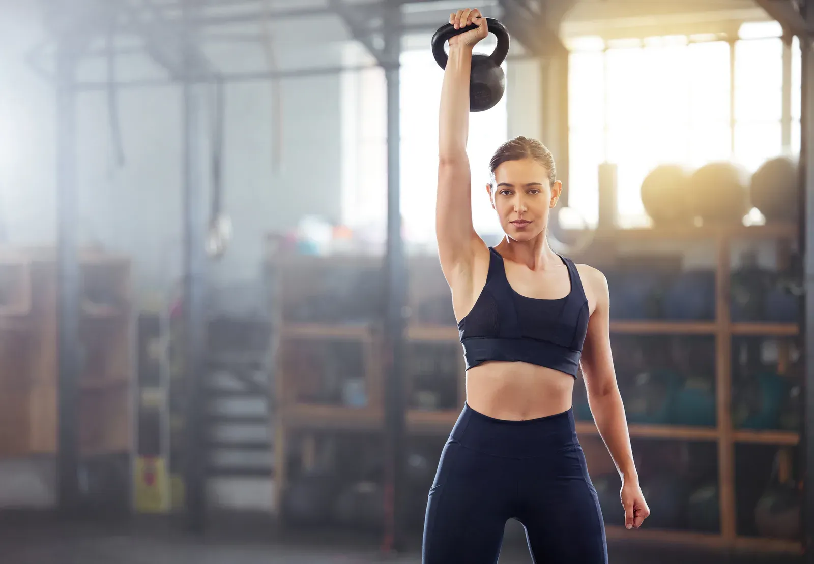 Strong woman doing a kettlebell lift in a gym, building strength without adding size