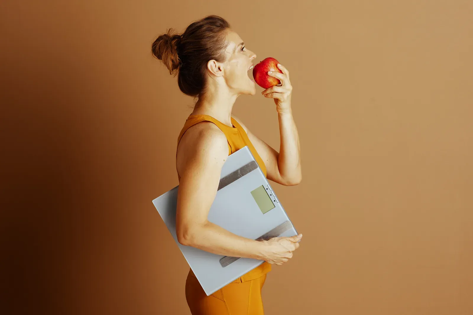 Woman holding an apple next to a scale while eating mindfully, a theme in weight loss and metabolism