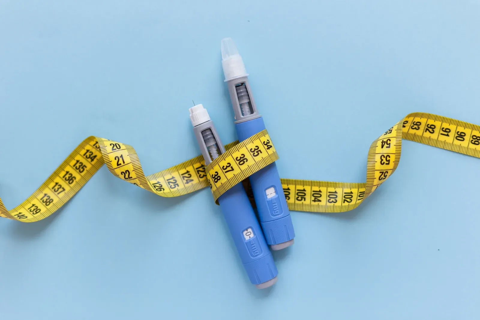 GLP-1 injector pens with a yellow measuring tape wrapped around them