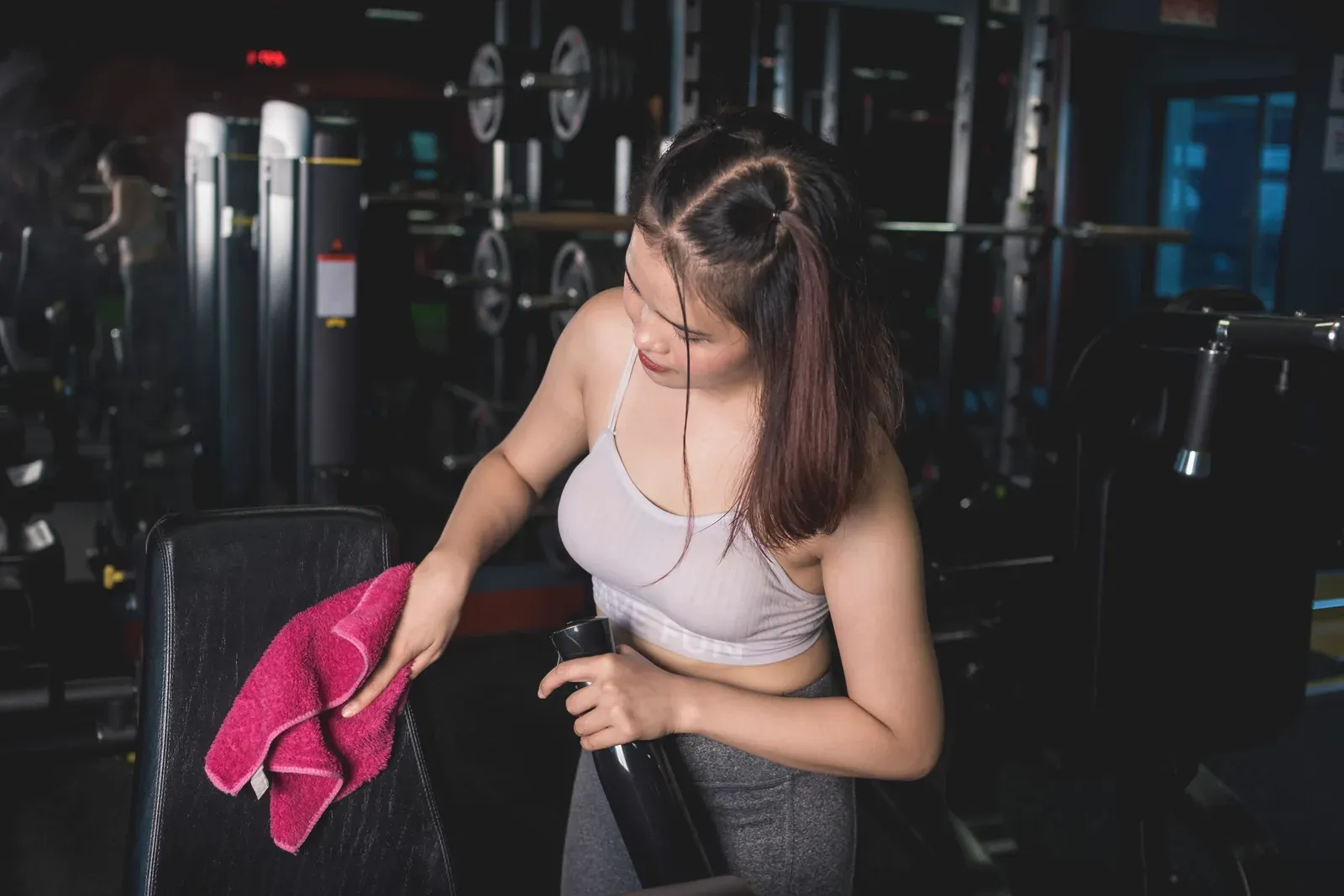 Young woman cleaning and sanitizing an incline bench with spray, a basic gym etiquette habit
