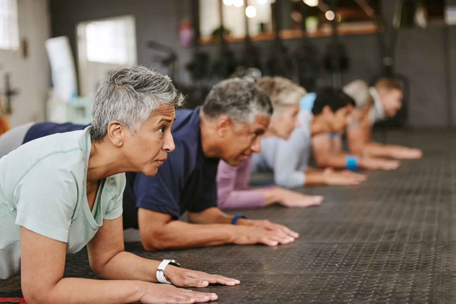 People doing a plank in a class at an indoor gym, a group workout compared with personal training