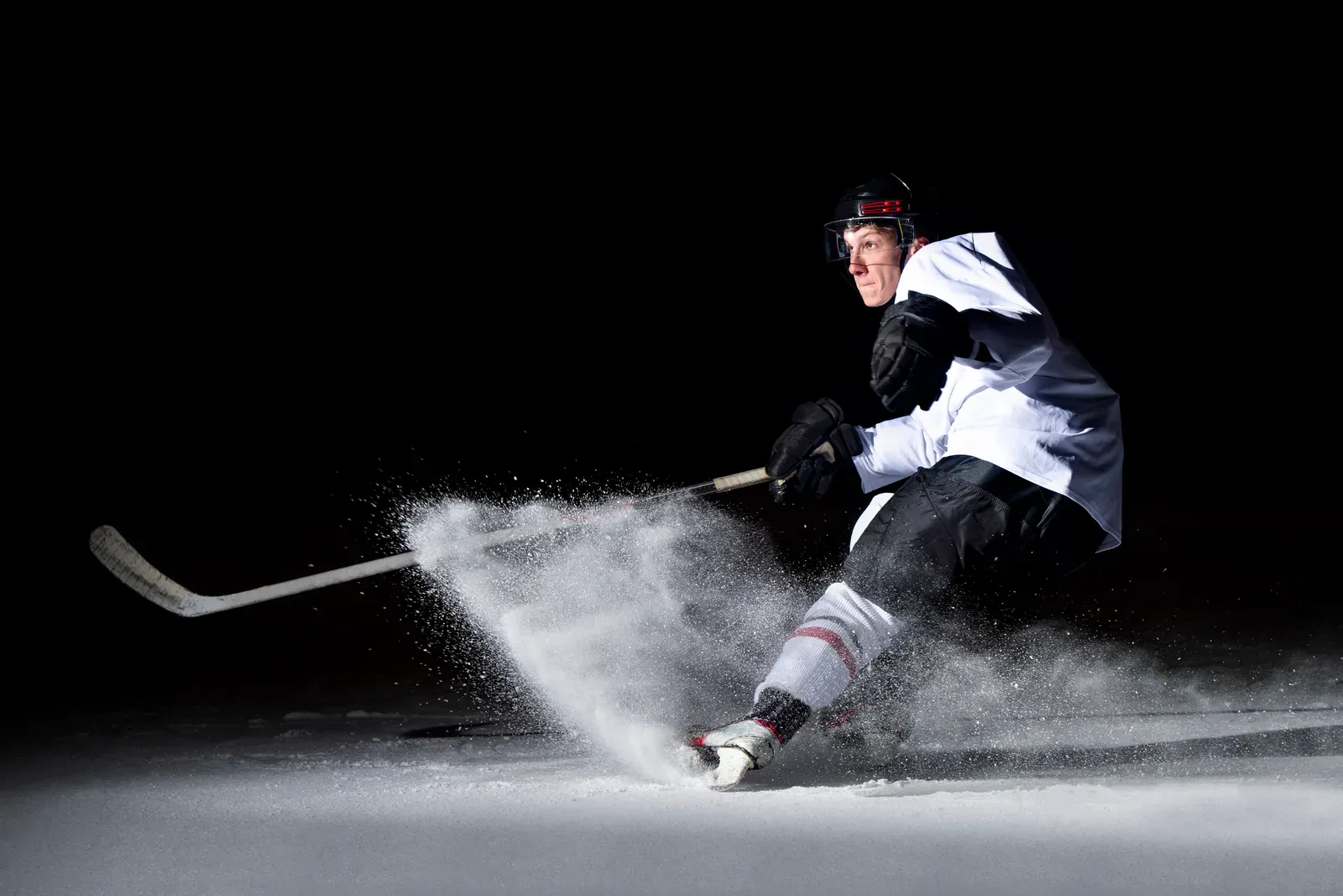 Hockey player leaning into a tight turn on the ice, snow spraying from the skates