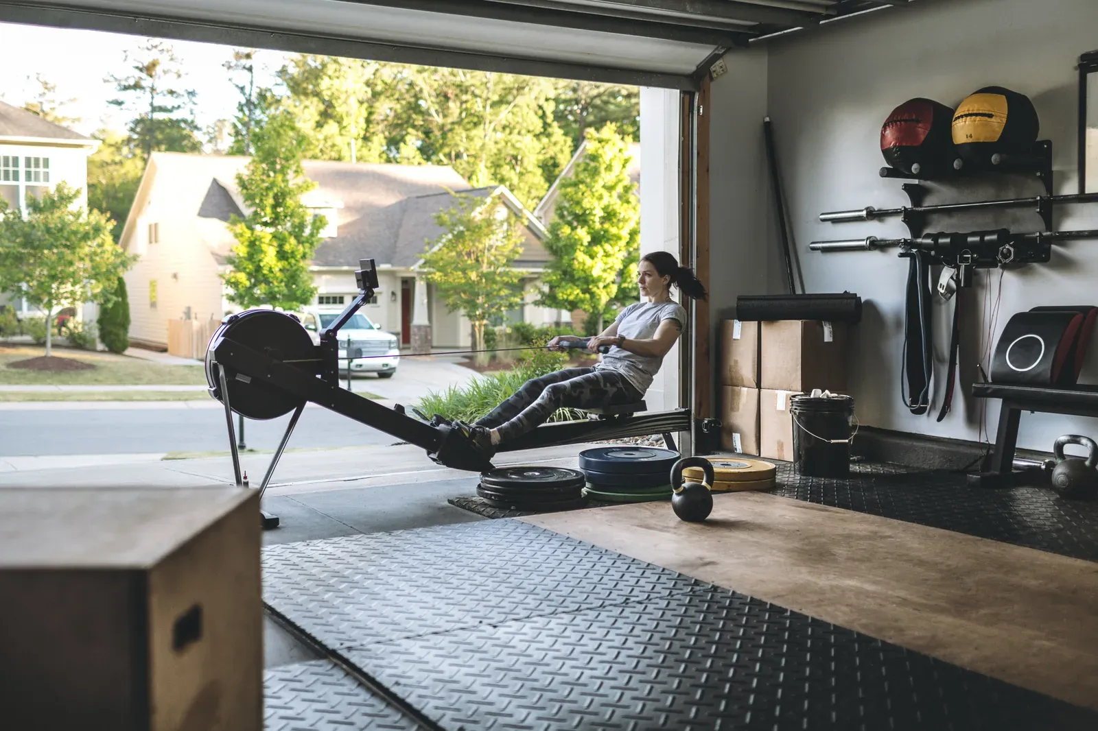 Active woman exercising on a rowing machine in her home garage gym, a home setup to weigh against membership