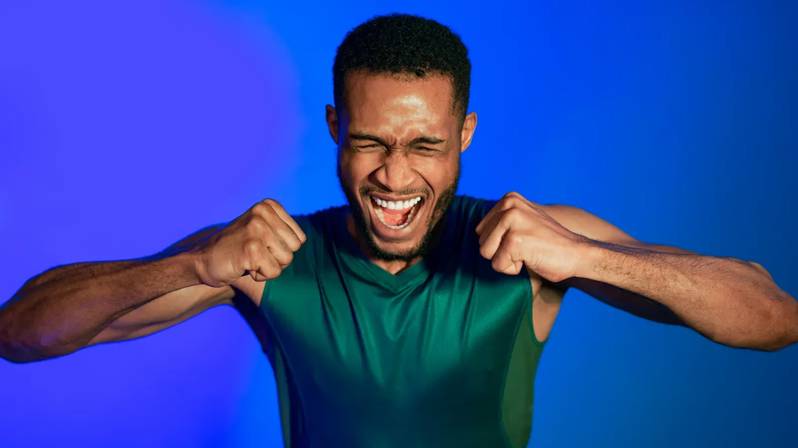 Sporty man shouting emotionally with clenched fists in a studio, the effort of training close to failure