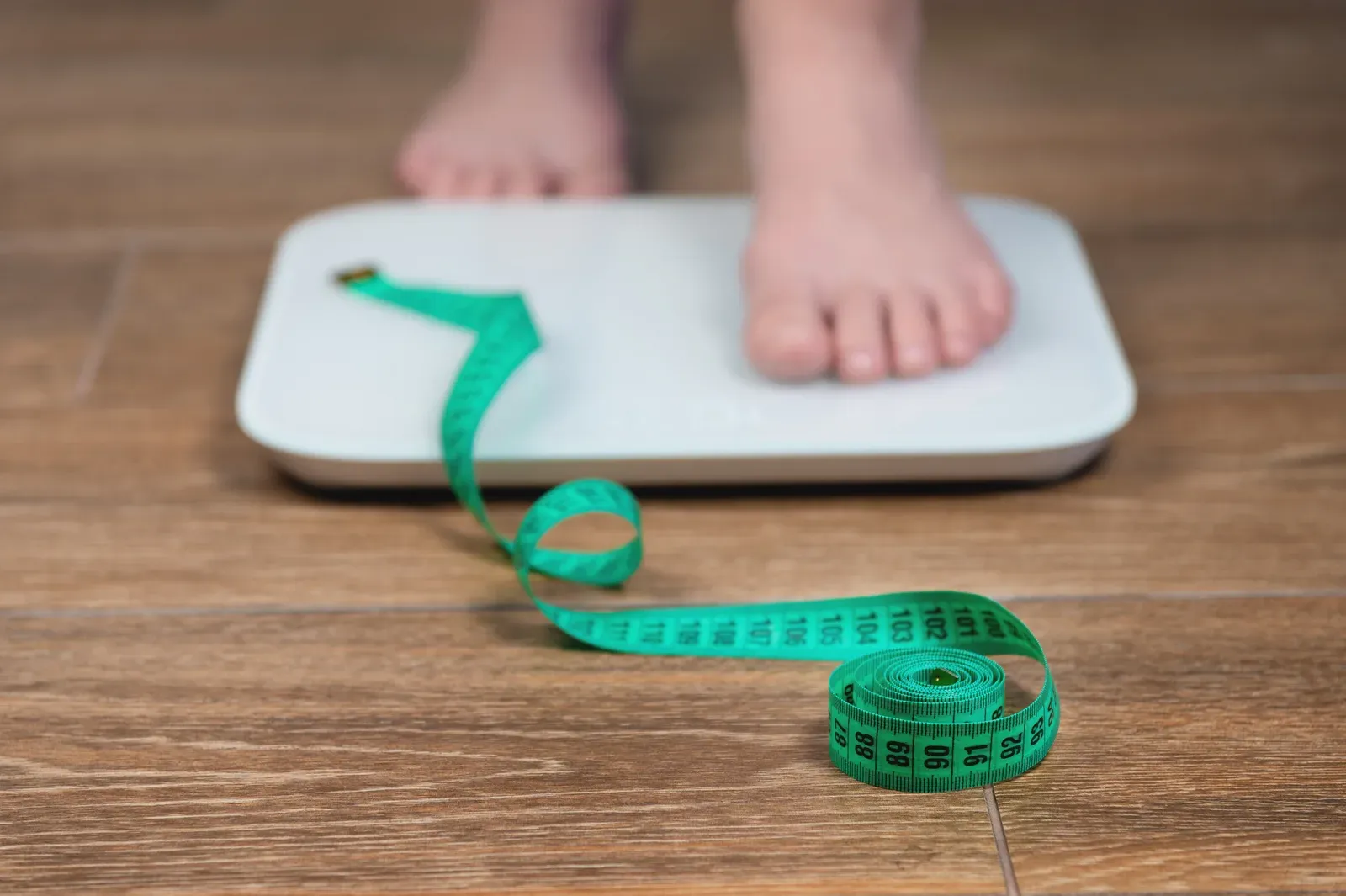 Woman standing on a scale with a measuring tape, tracking body fat change over weeks