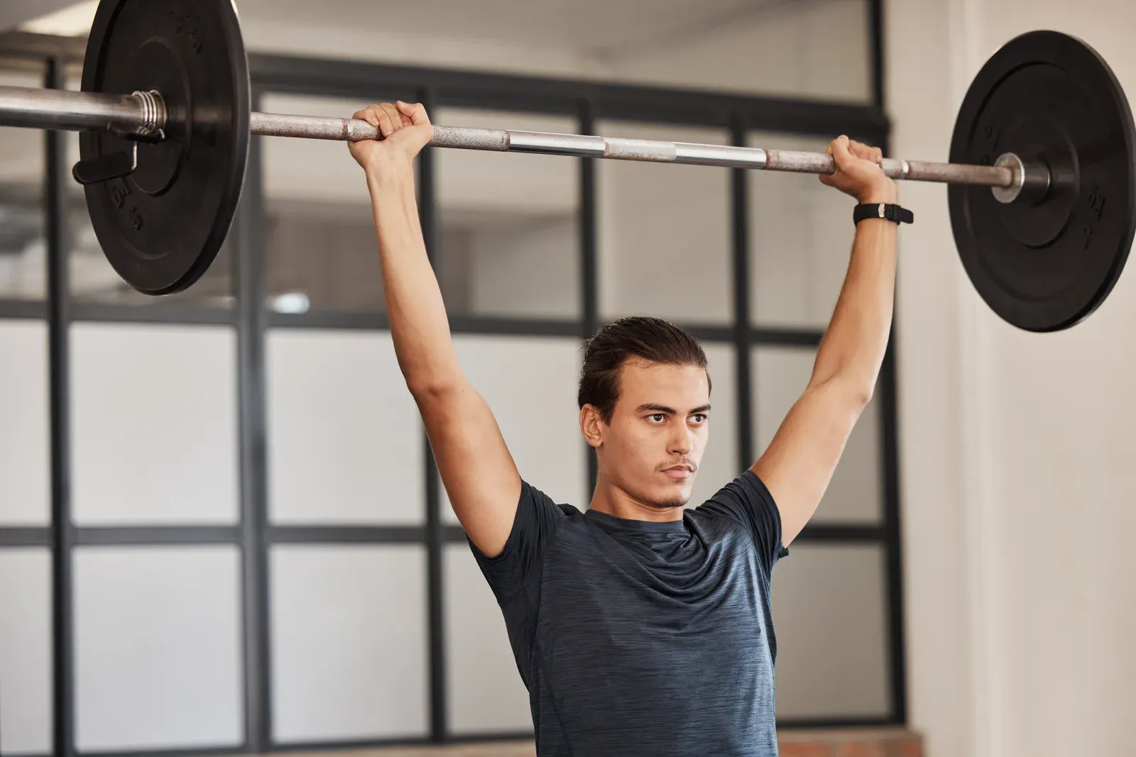 Strong man holding a barbell overhead in a sports club, a strength exercise for men building muscle over 40