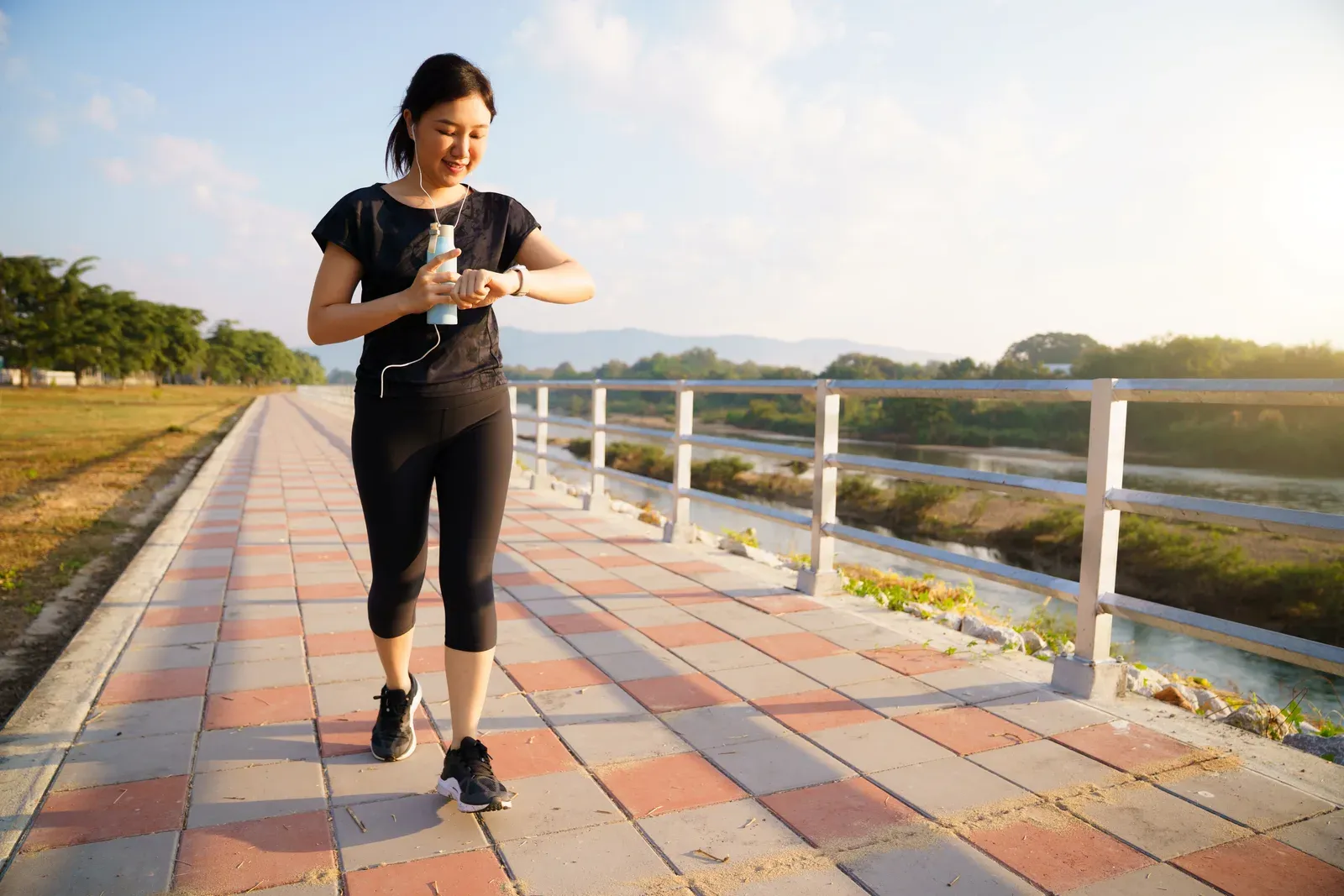 Young woman checking her smartwatch while exercising in a riverside park, tracking a workout's length