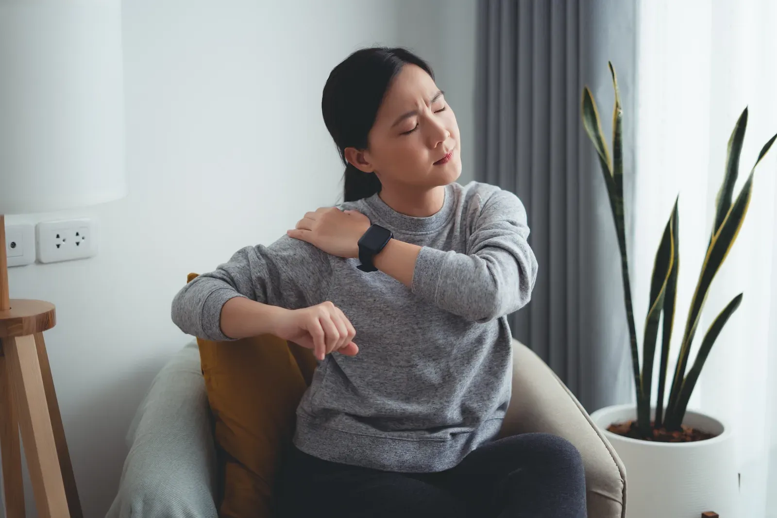 Woman resting in an armchair at home with a sore shoulder