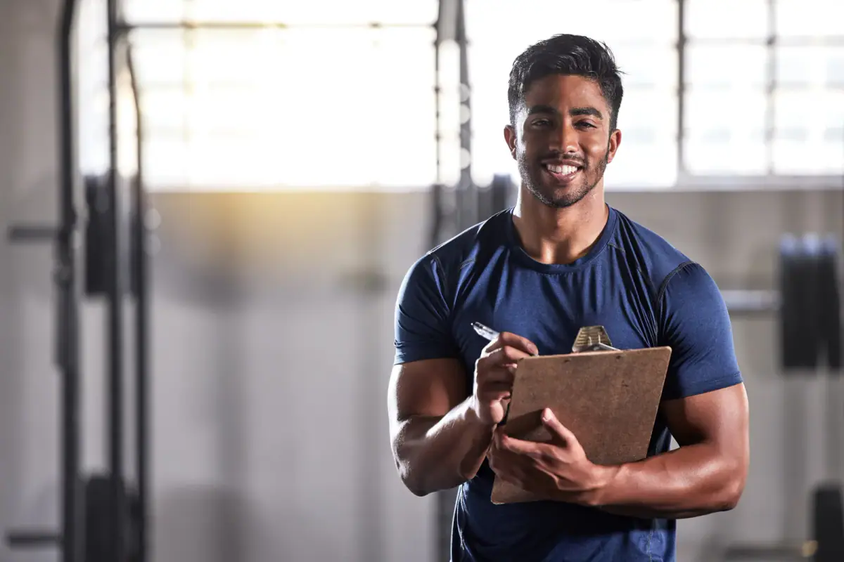 Smiling personal trainer holding a clipboard to log a client's gym progress