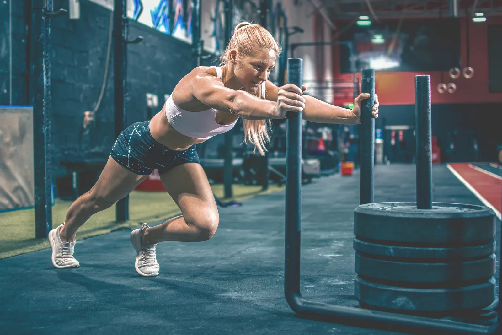 Young sportswoman pushing a prowler sled in the gym, a staple of hybrid fitness race training