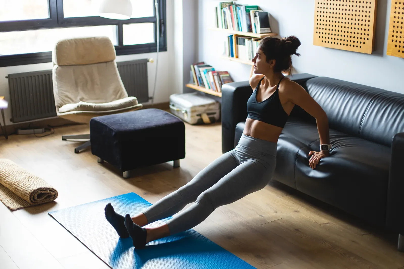 A trainer coaching a client through dumbbell exercises in a living room with limited equipment