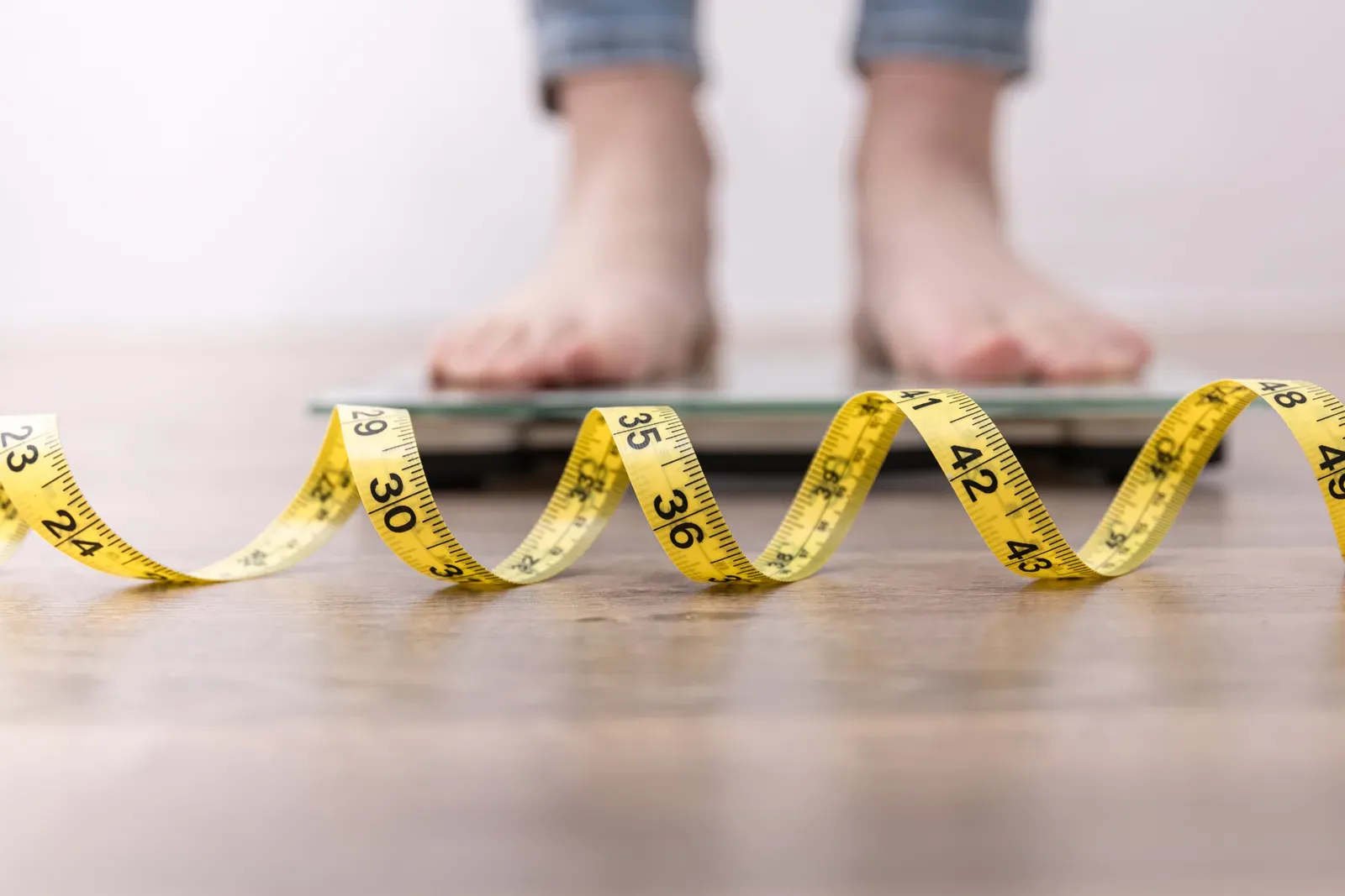 Stepping onto a bathroom scale beside a tape measure to check weight loss