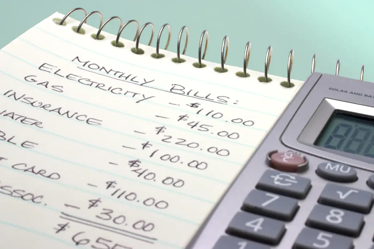 Adding up monthly bills on a notepad with a calculator to budget for training