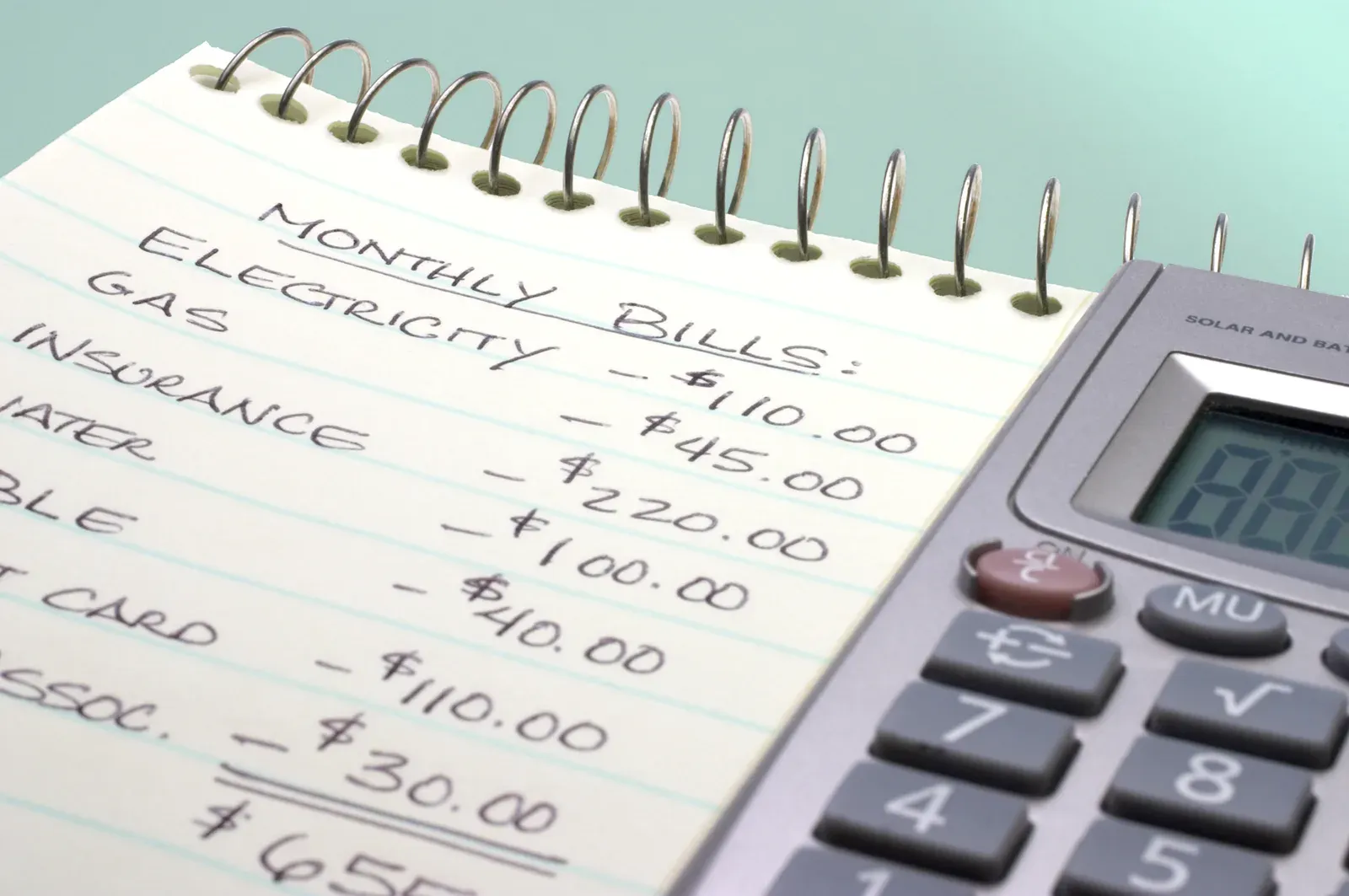 Adding up monthly bills on a notepad with a calculator to budget for training