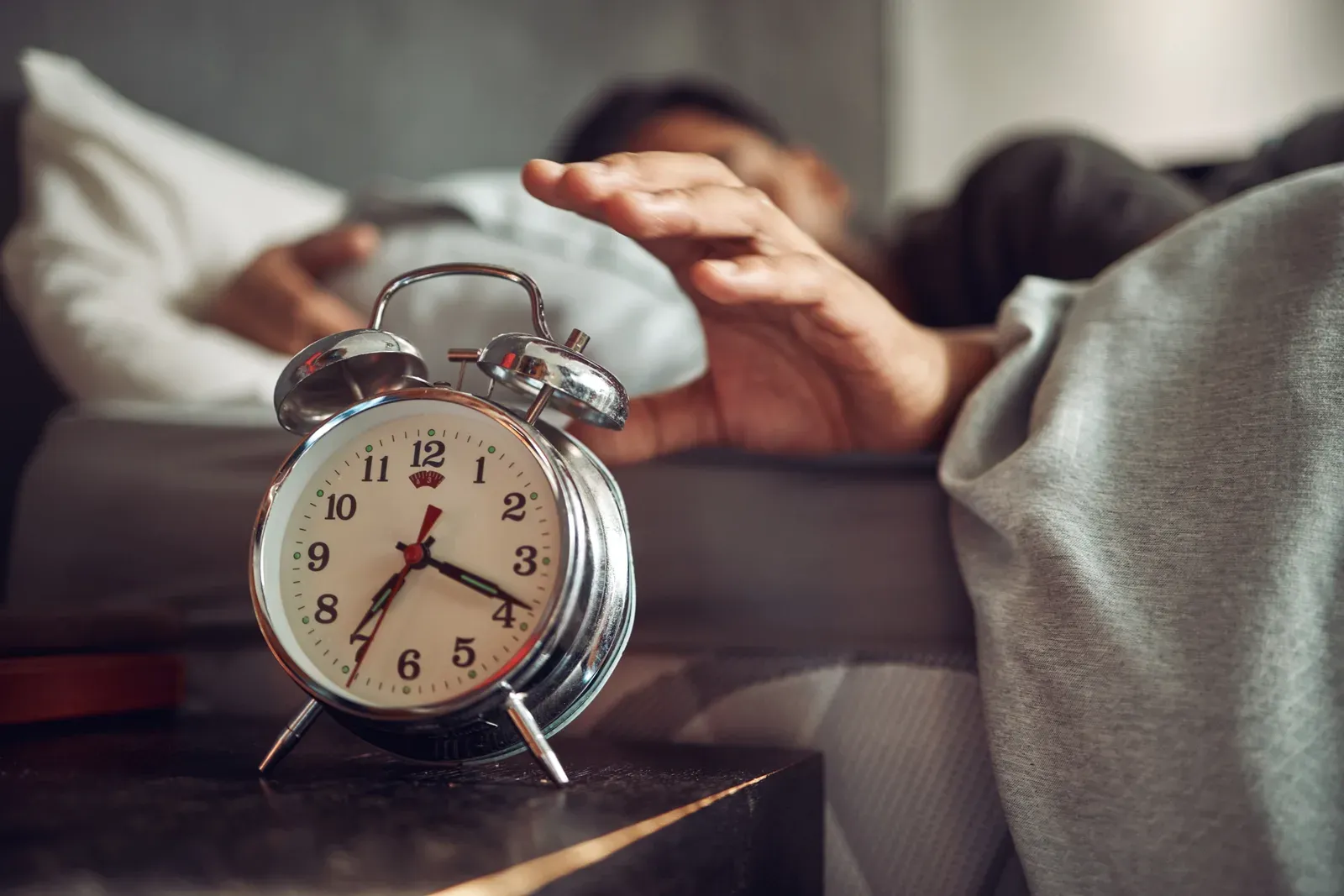 Young man reaching for his alarm clock after waking up in bed