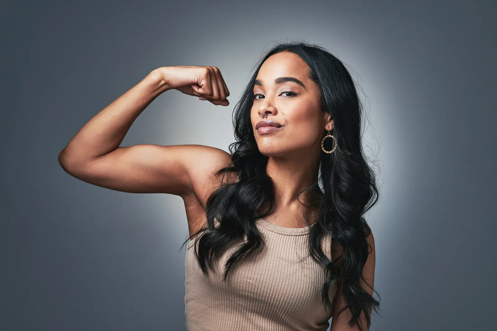 Young woman flexing her arms in front of a grey studio backdrop