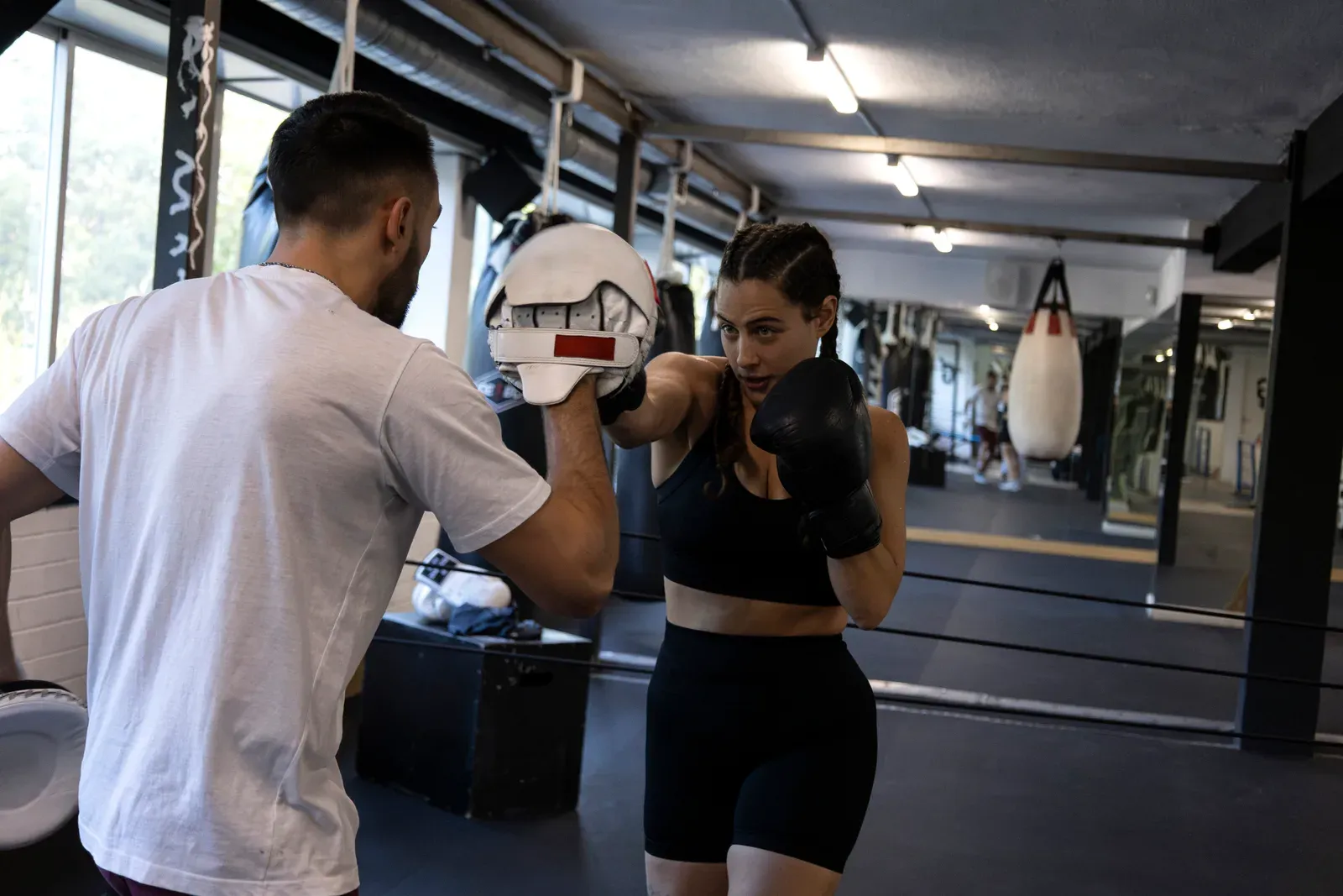 Woman boxer training with a coach hitting focus pads, coached bag and pad work