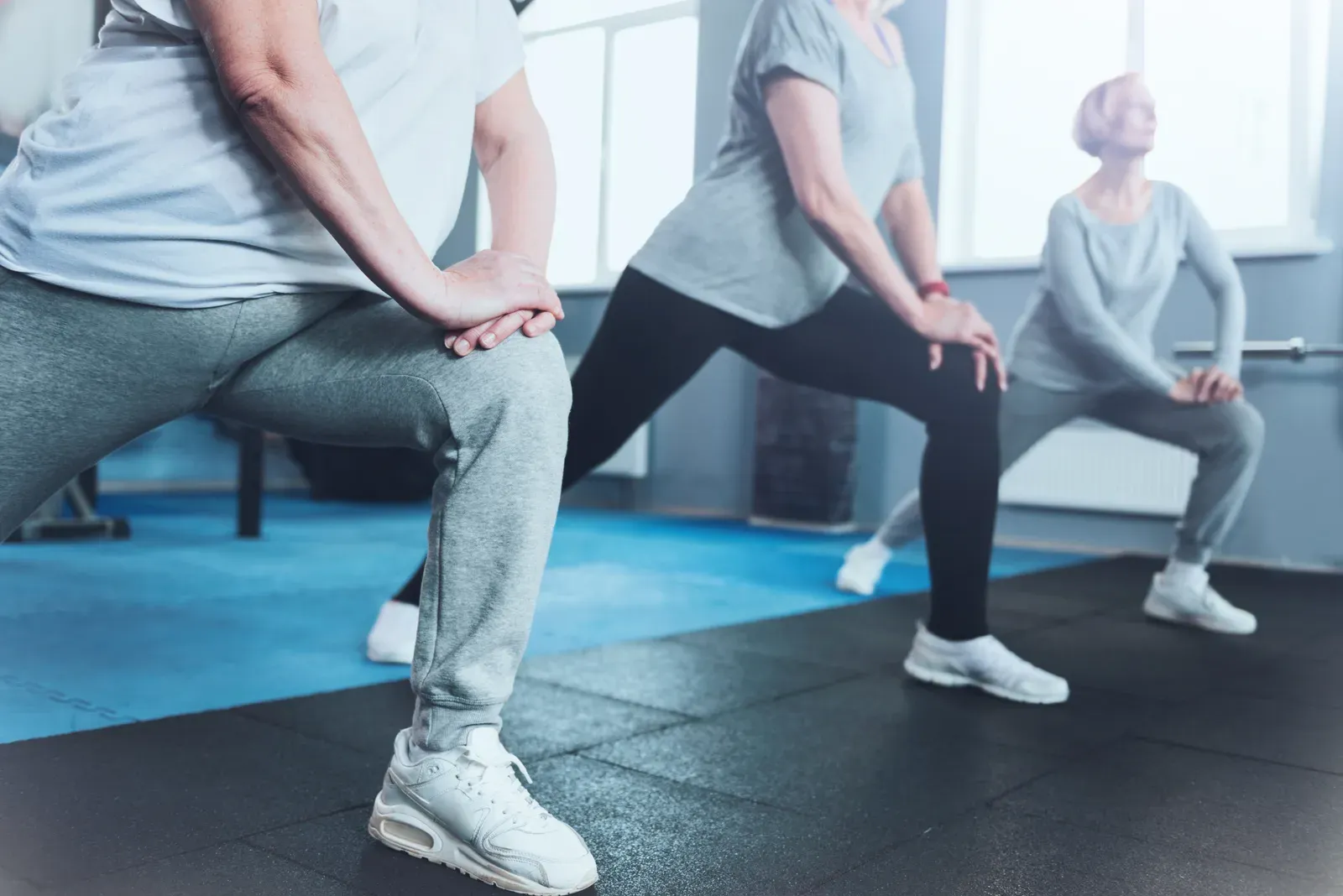 Older man performing a supported step-up exercise while a coach stands close by