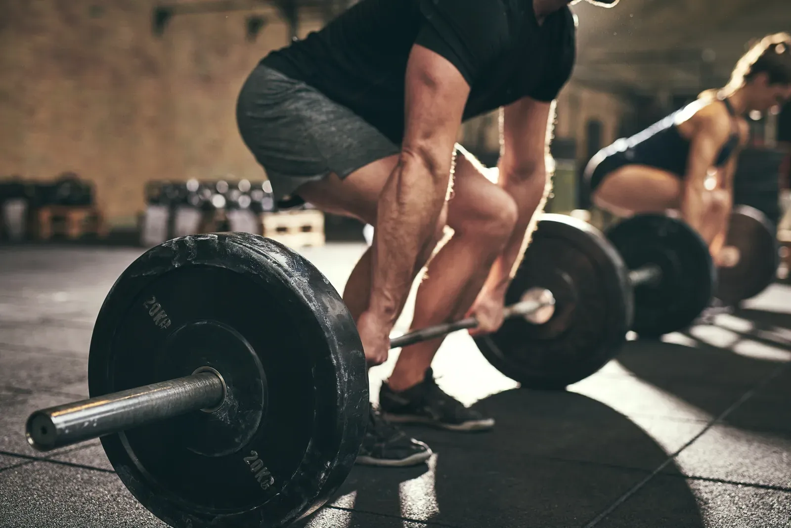 A middle aged man performing a barbell deadlift with a coach observing his form