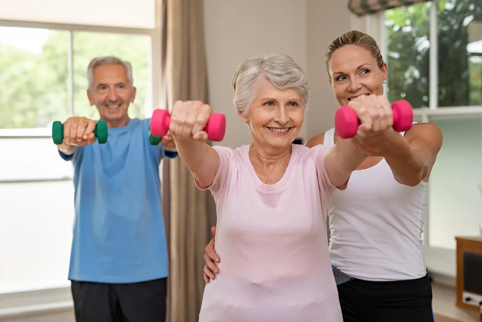 Coach guiding an older woman through a supported dumbbell squat in a bright training room