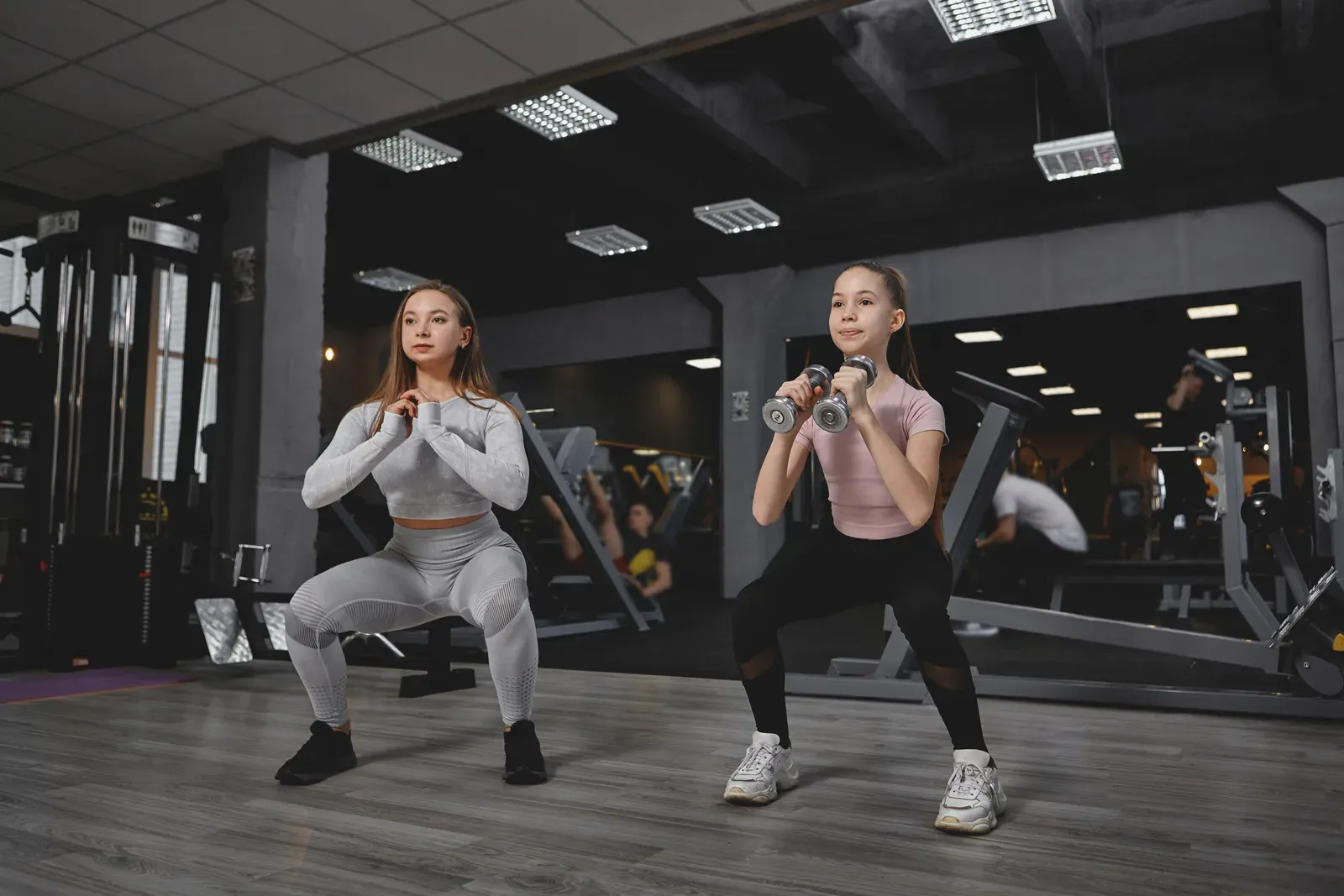A teenager learning a goblet squat with a coach guiding form in a private training room