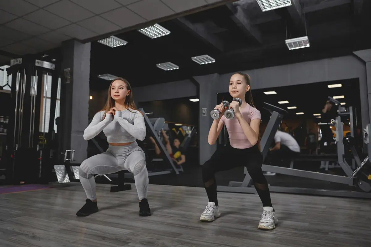 A teenager learning a goblet squat with a coach guiding form in a private training room