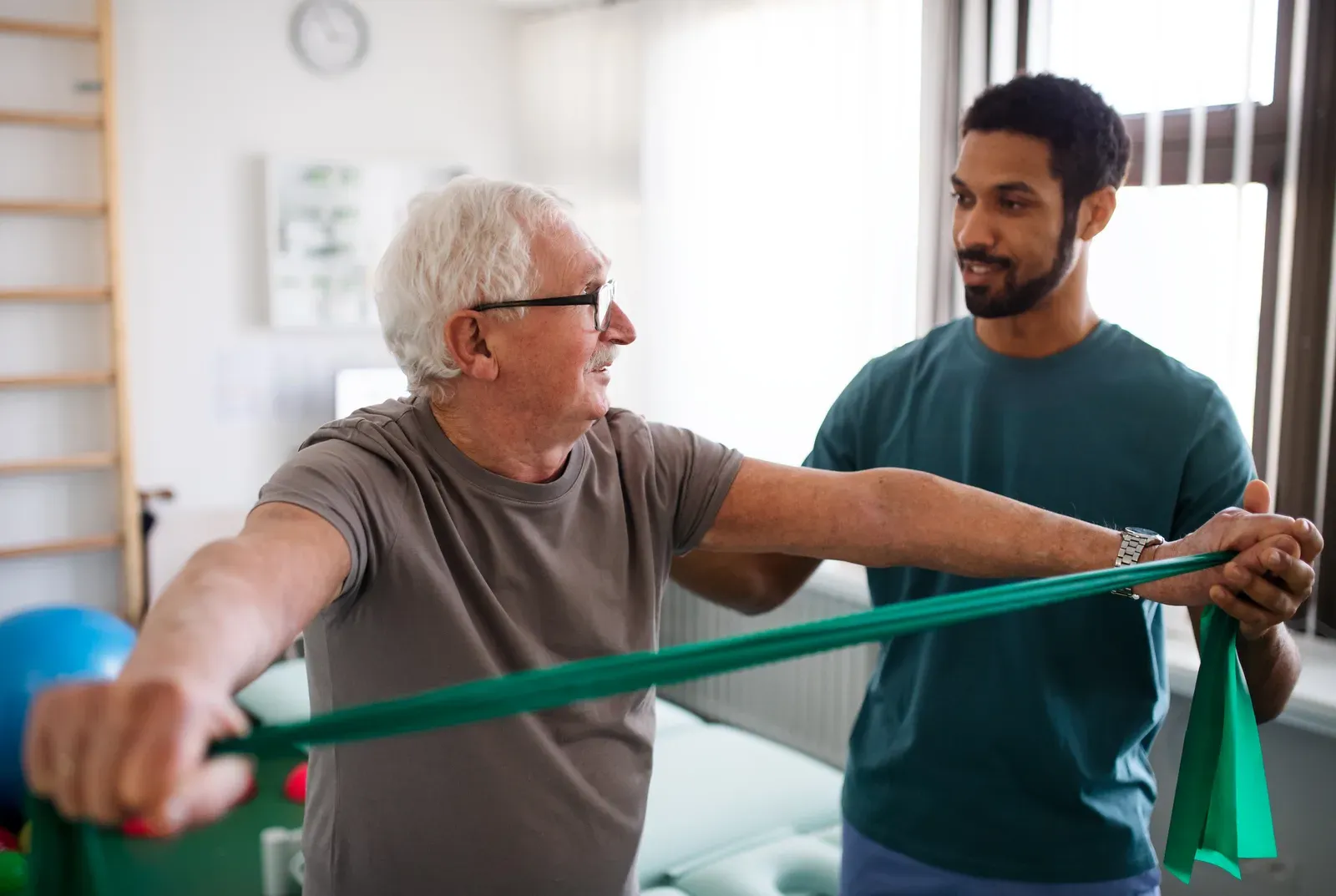 Young physiotherapist exercising with a senior patient in a physio room, care to weigh against personal training
