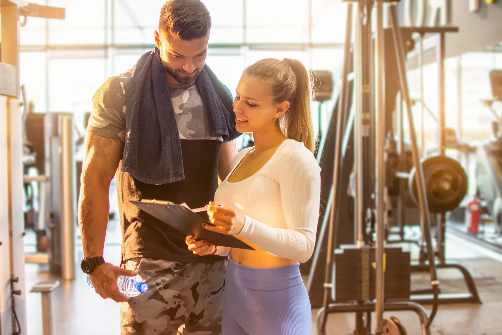 Female personal trainer showing exercise progress to a male client at the gym, with coaching bundled with nutrition
