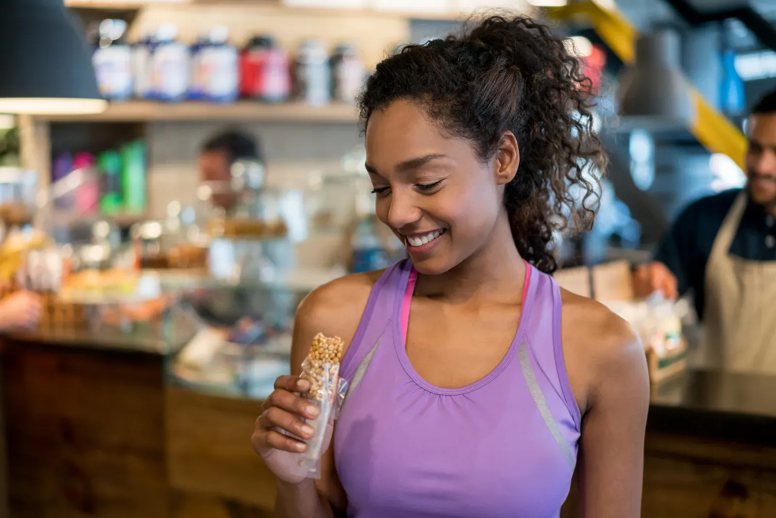 Woman eating a protein bar at the gym, a snack that adds to daily protein for women who lift
