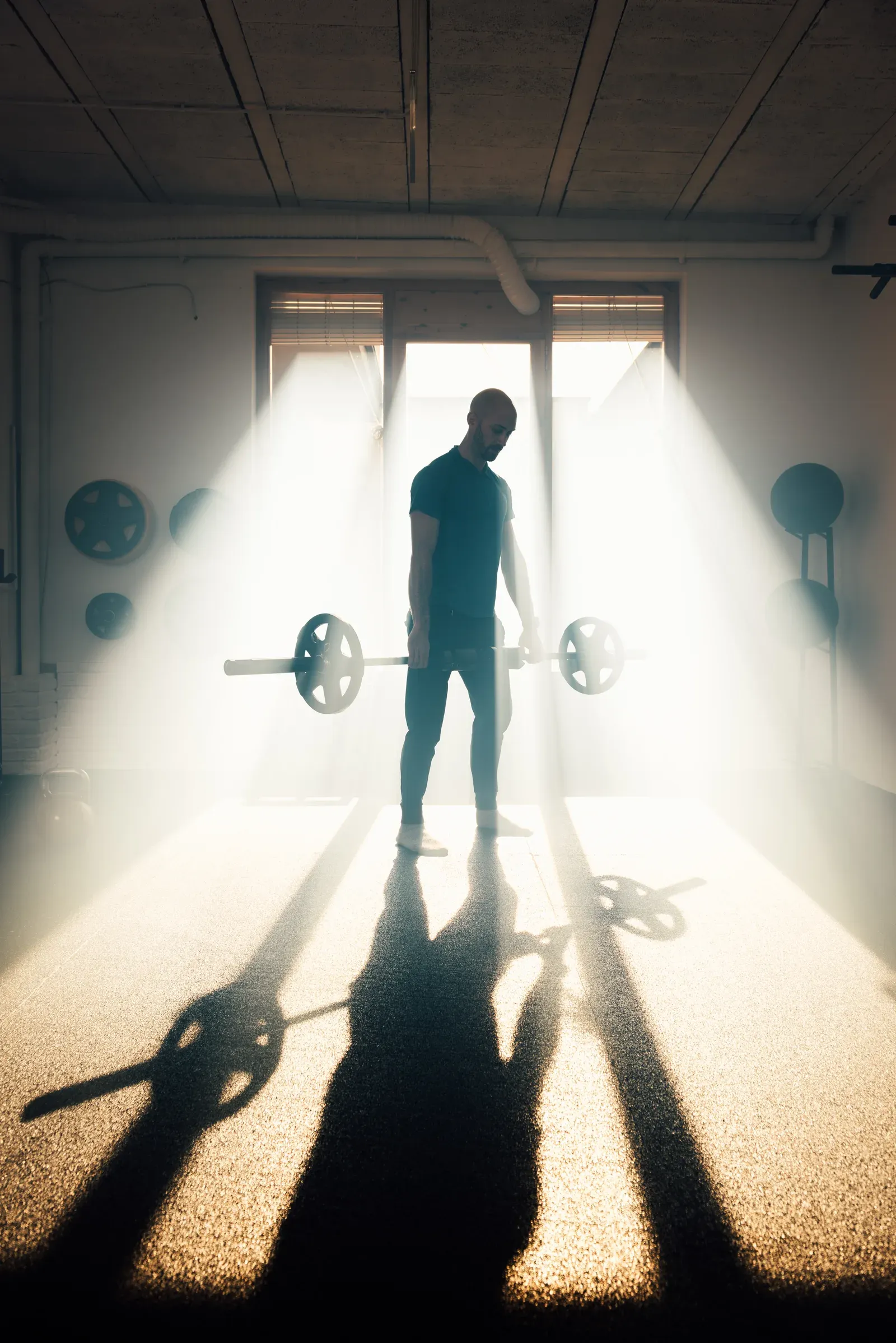 Backlit man holding a barbell in the gym, the effort behind three weekly workouts