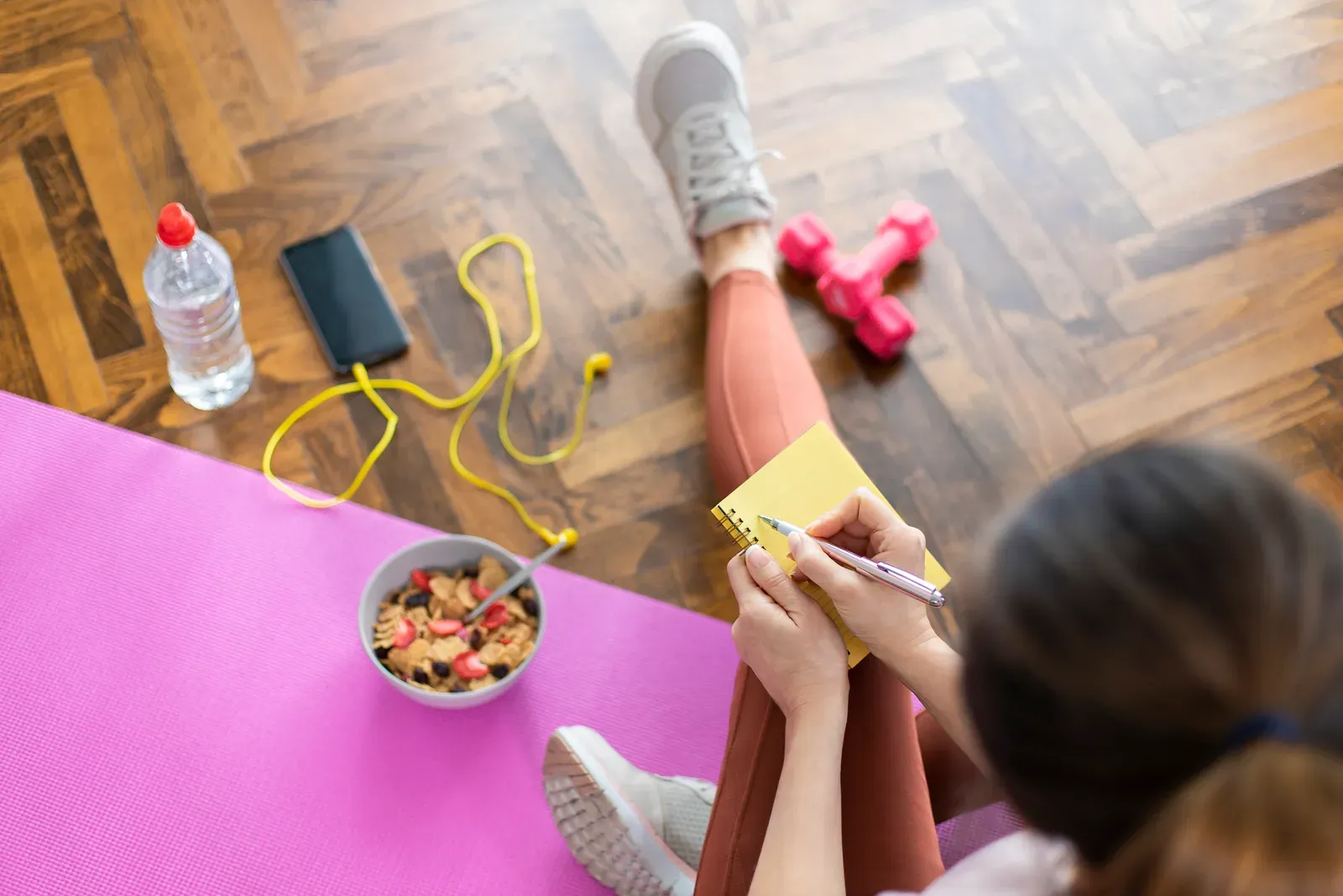 Young sporty woman writing a workout plan in a notebook after a workout, setting fitness goals