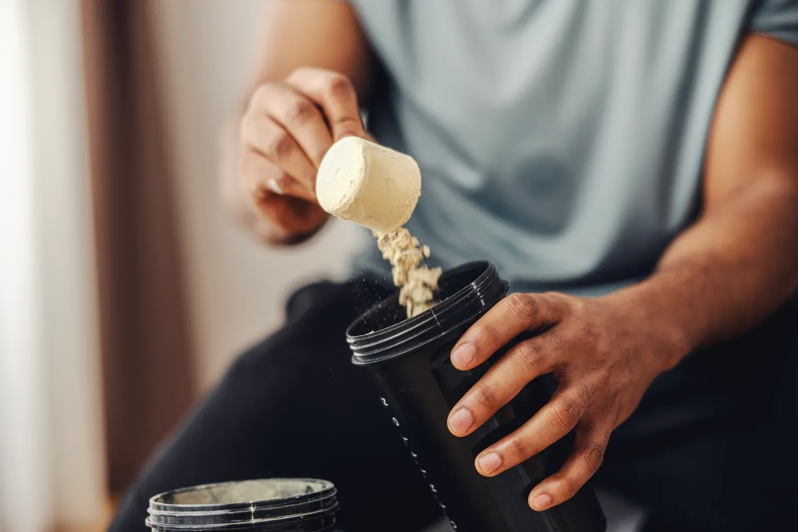 Adding a scoop of supplement powder to a shaker bottle
