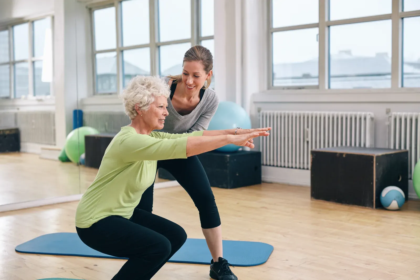 An older woman performing a goblet squat beside a coach