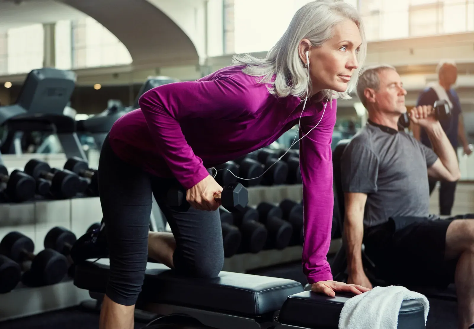 A woman in her fifties strength training with dumbbells alongside a coach