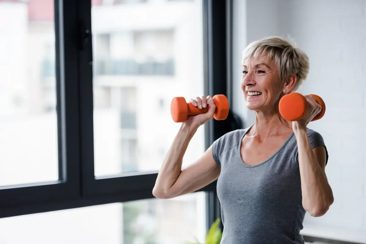 An older client performing a gentle dumbbell exercise under a trainer's watch