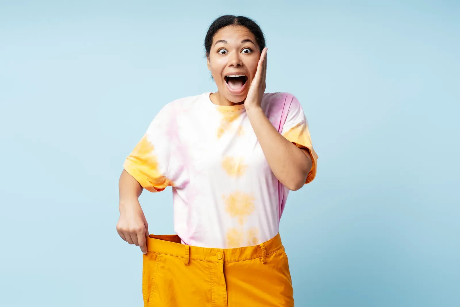 Excited woman holding out her now loose pants after losing weight