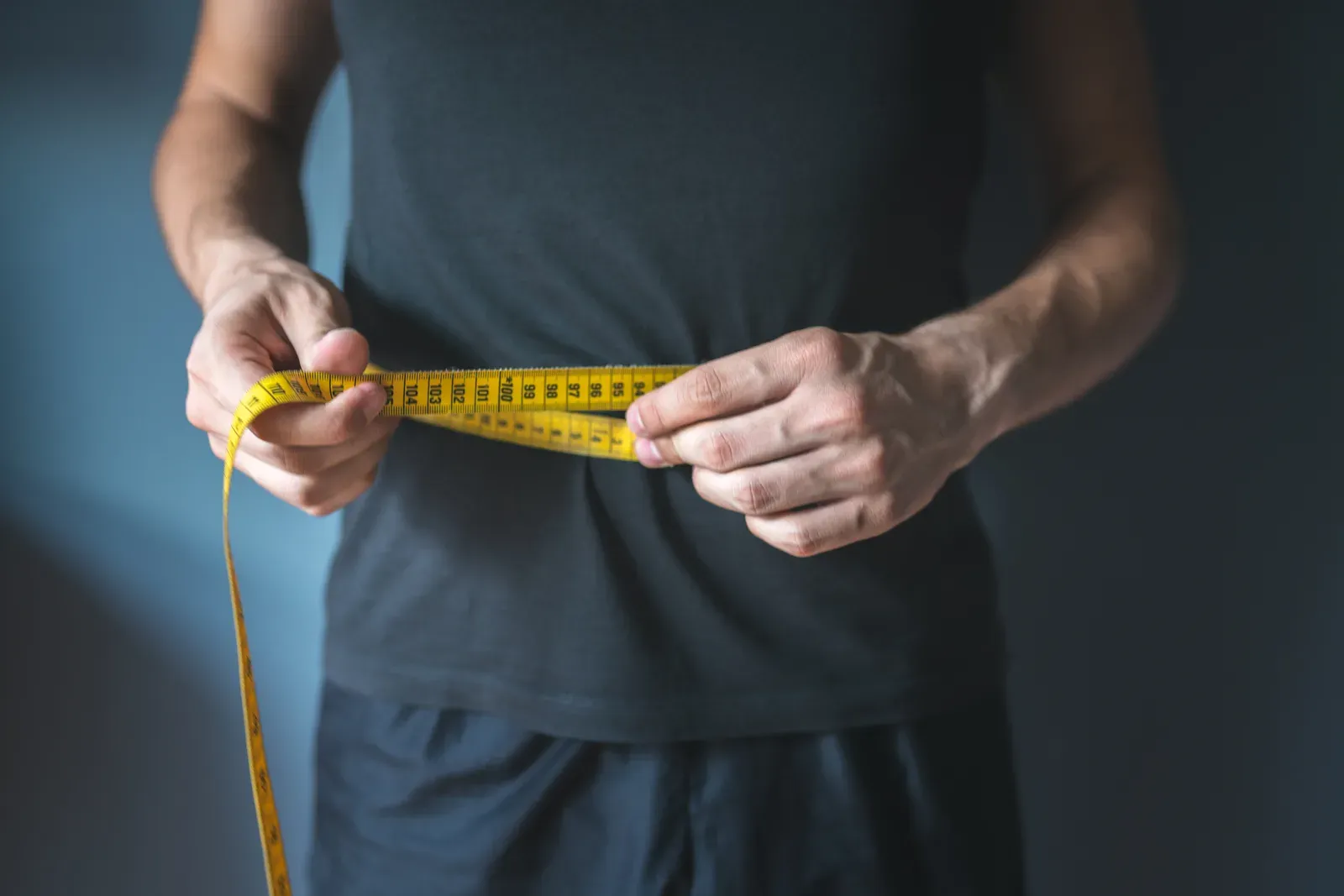 Slim man measuring his waist with a tape to check belly fat