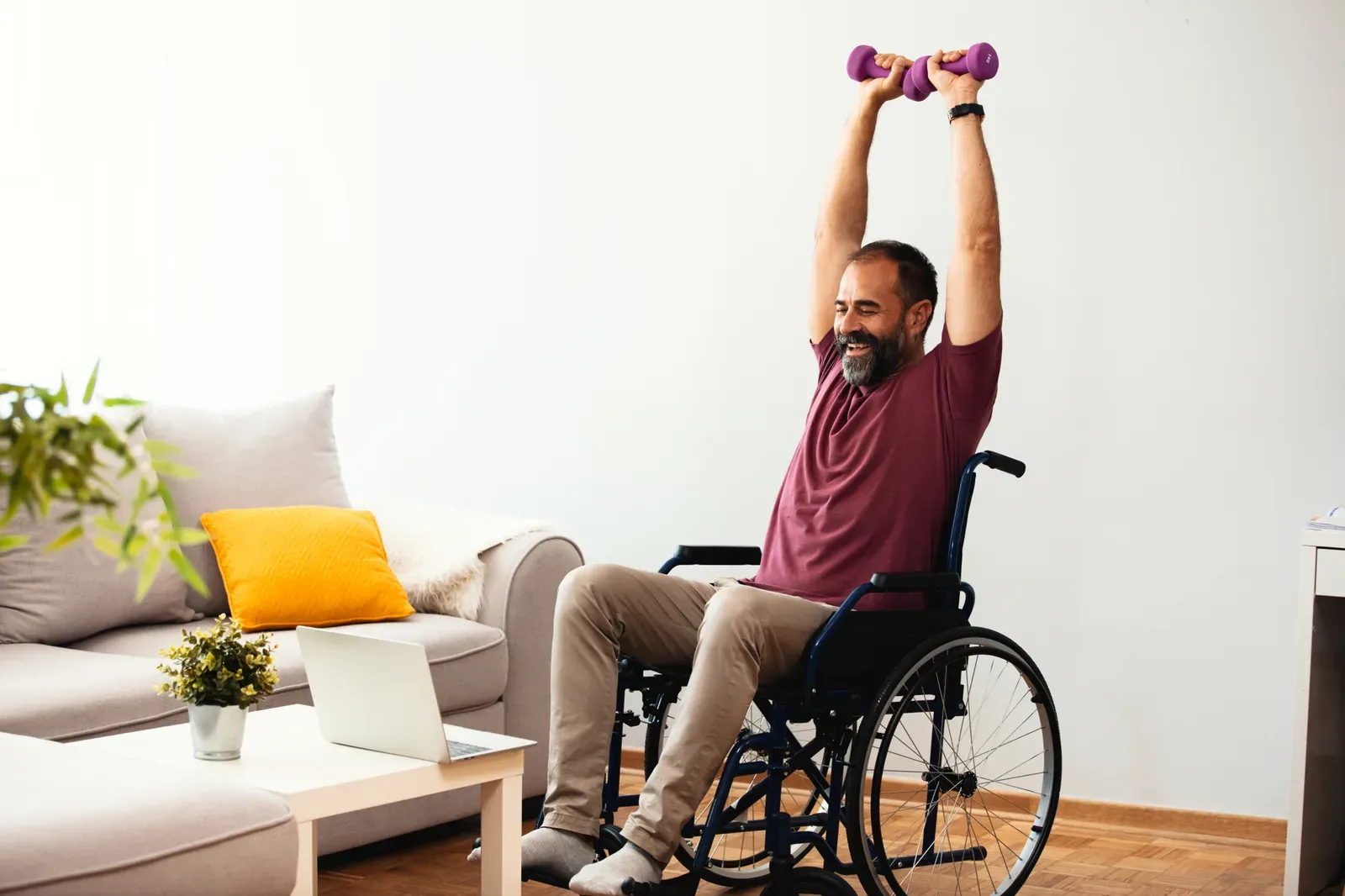 A man in a wheelchair doing a cable row exercise with guidance from a trainer